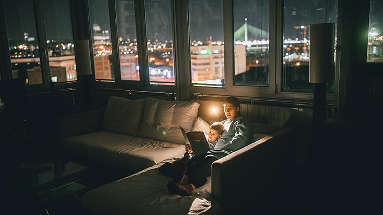 A mother reads to her son in the living room at night