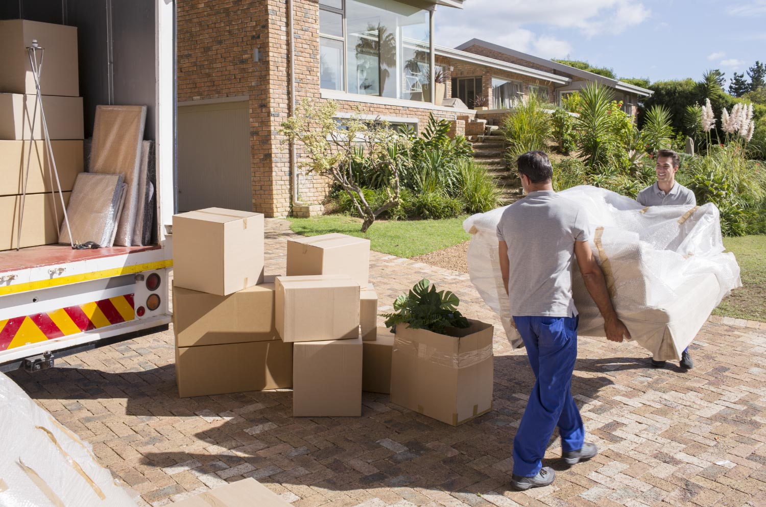 Movers carry sofa from moving truck to house