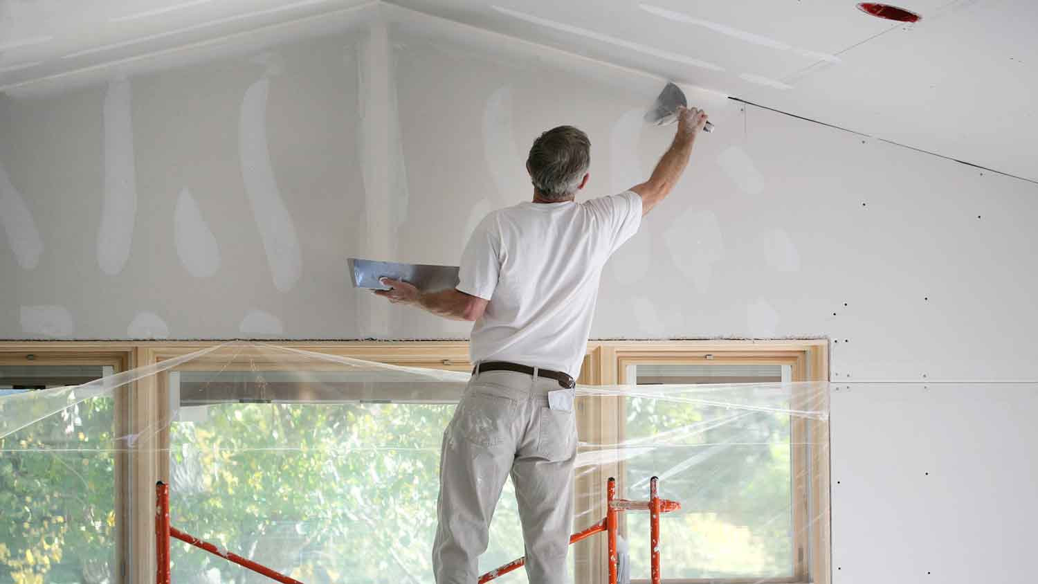 Worker on a scaffolding mudding interior drywall