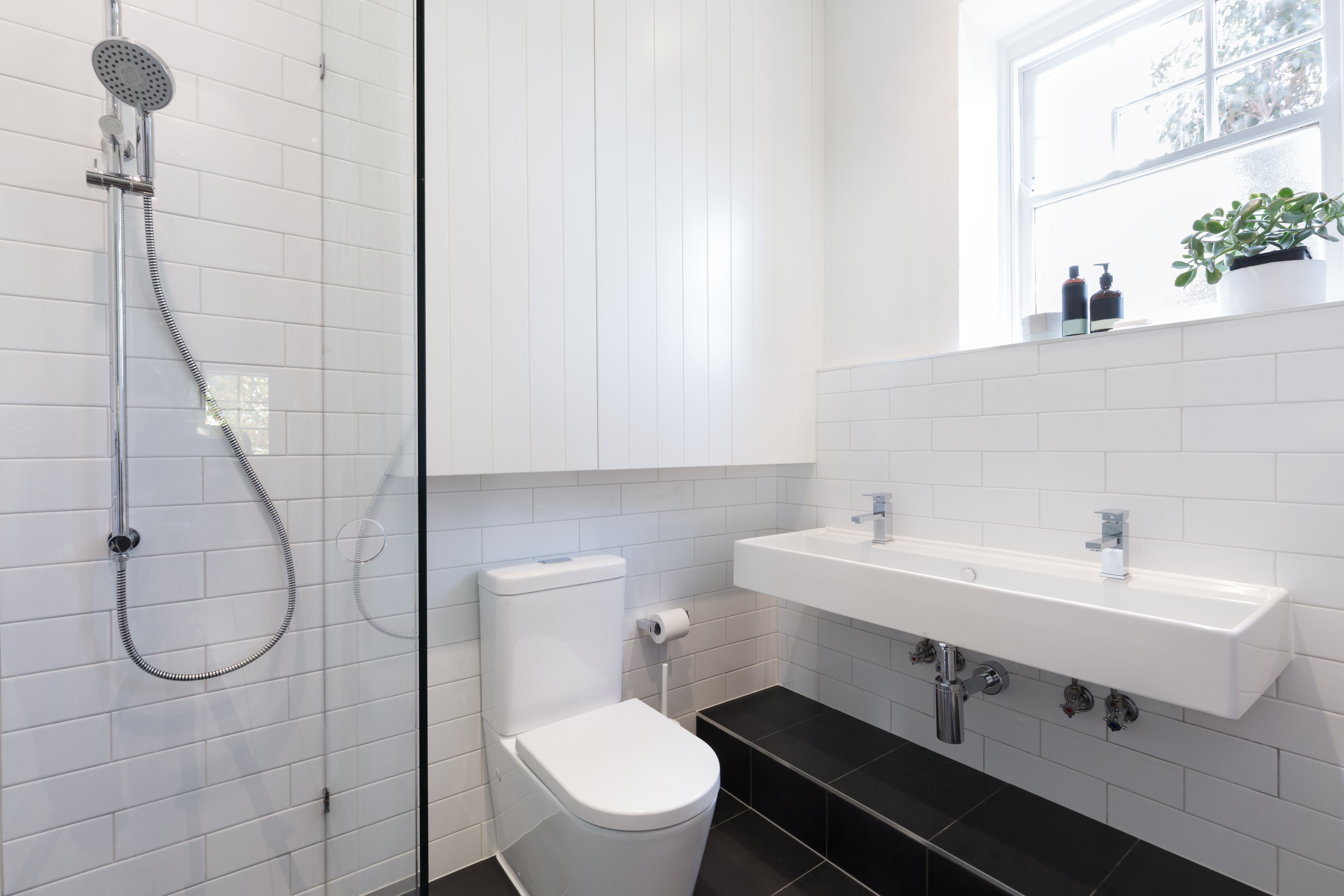 Black and white bathroom with white tile walls, black tile floors, standup shower, and narrow double-basin vanity