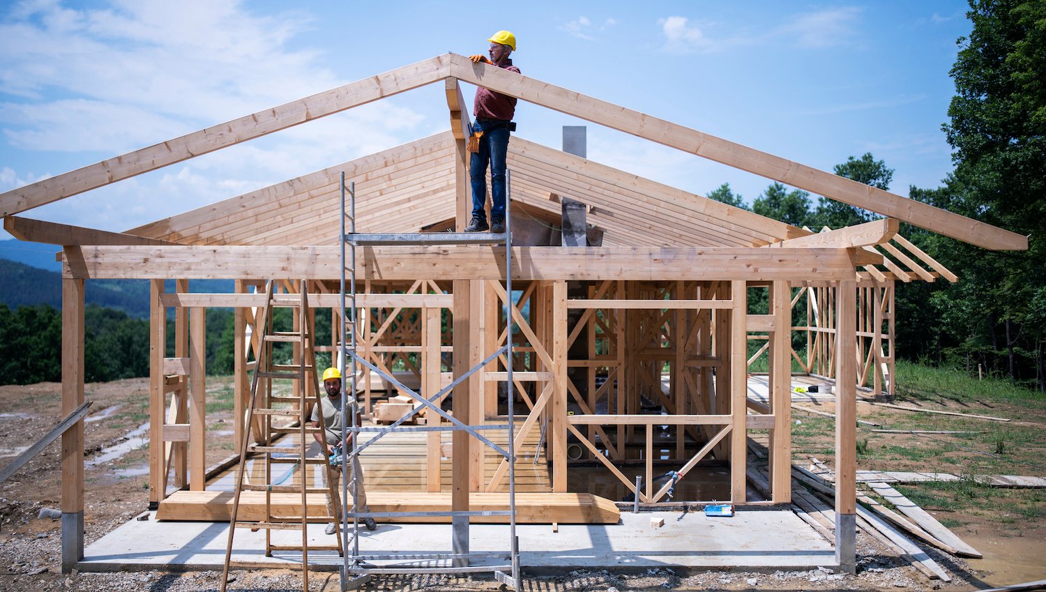 two construction workers work on the wooden frame of a new house build