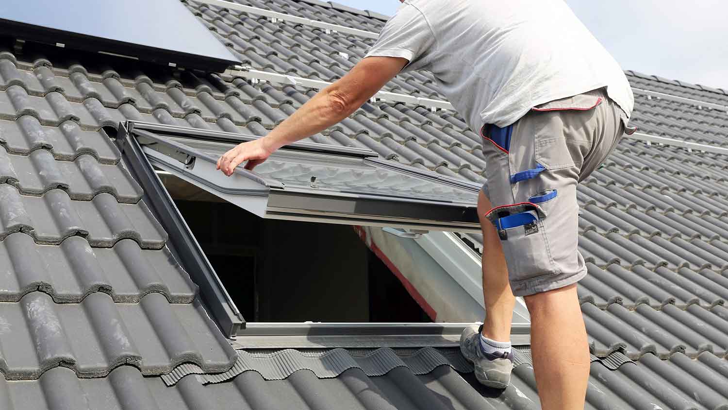 Worker standing on a roof installing a skylight