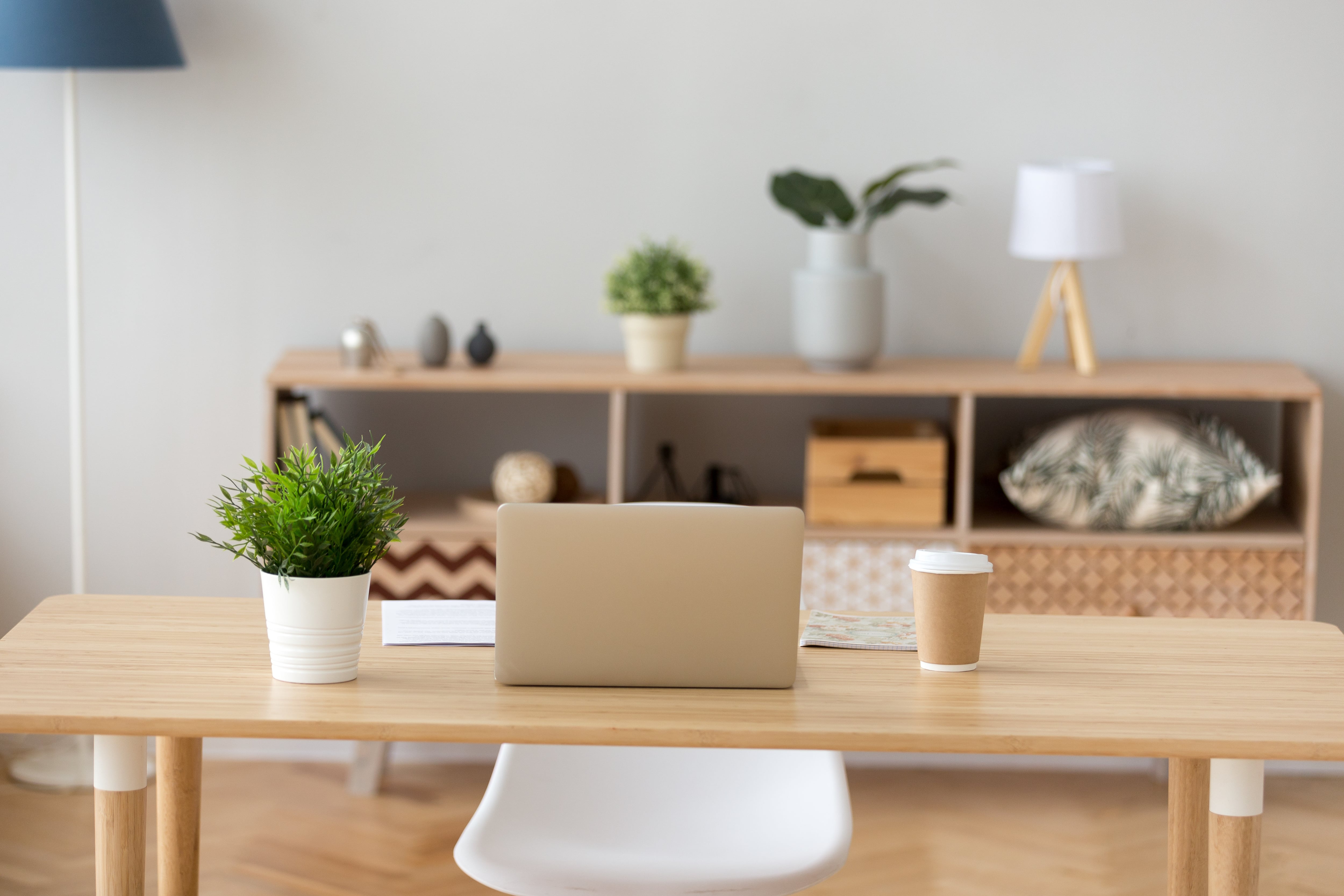 Minimalist home office with wooden table, white chair, bookshelf, and laptop