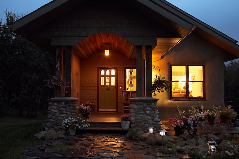 shot of front of house with outdoor light above front door, with light streaming out of front windows into dark front yard