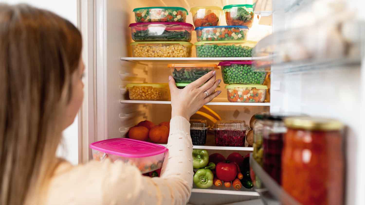 Woman arranging food in overcrowded fridge