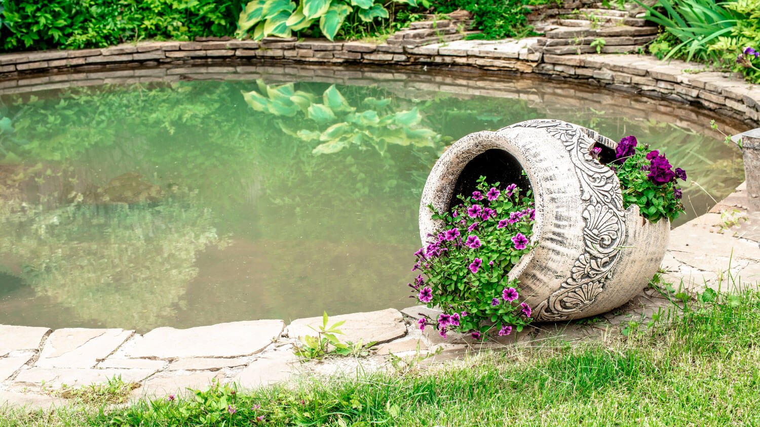 overturned pot with flowers in it next to small fish pond 