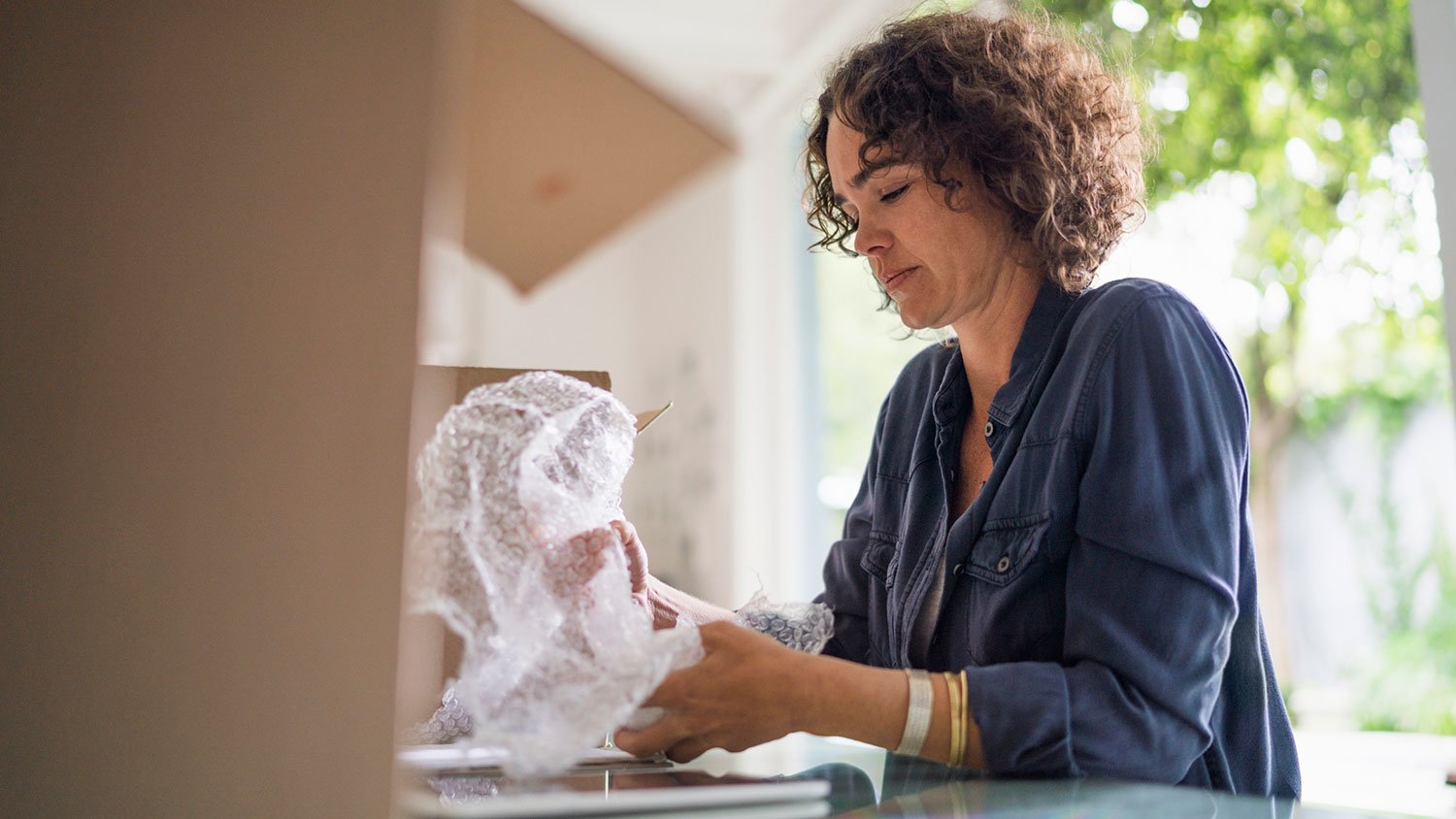 Woman packing fragile object with bubble wrap