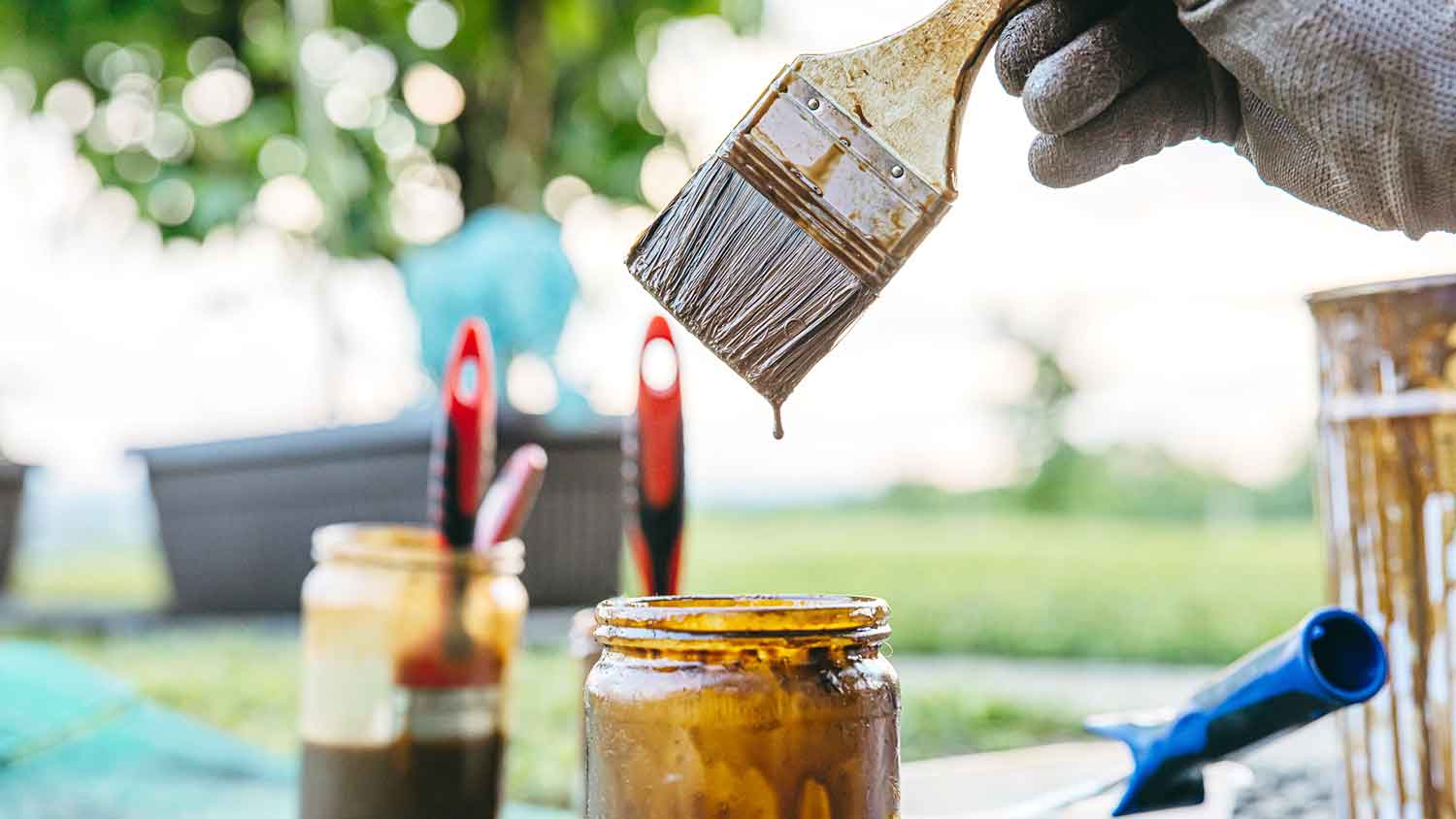 Hand holding brush with paint dripping into a jar