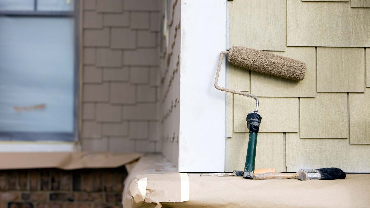 A paint roller and a brush standing against fiber cement siding