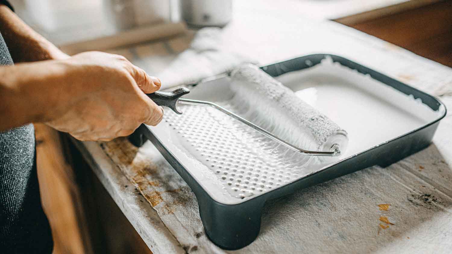 Handyperson dipping roller in a tray with paint