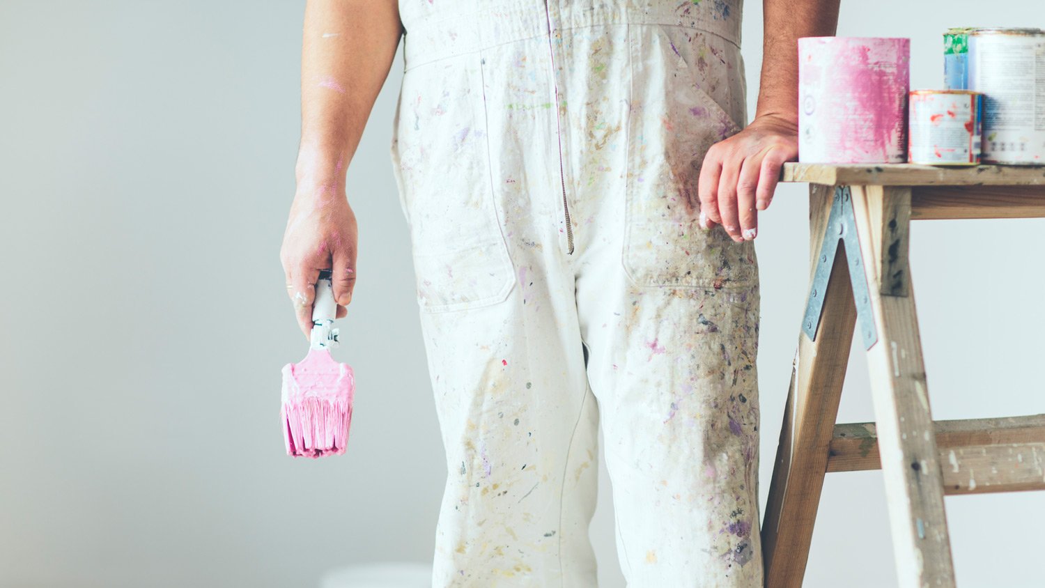 Painting wearing coveralls and standing next to paint supplies.