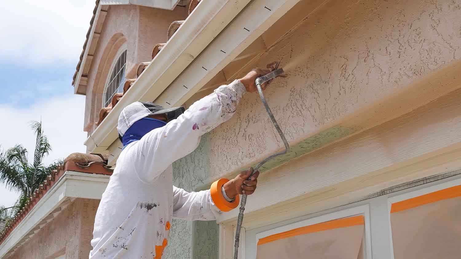 Professional painter using spray gun to paint stucco wall