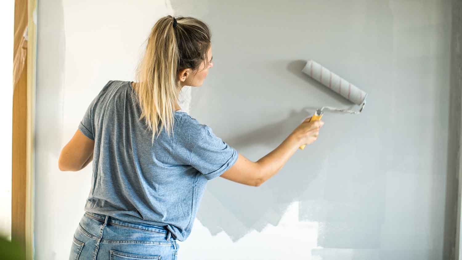 Woman using a roller to paint an interior wall