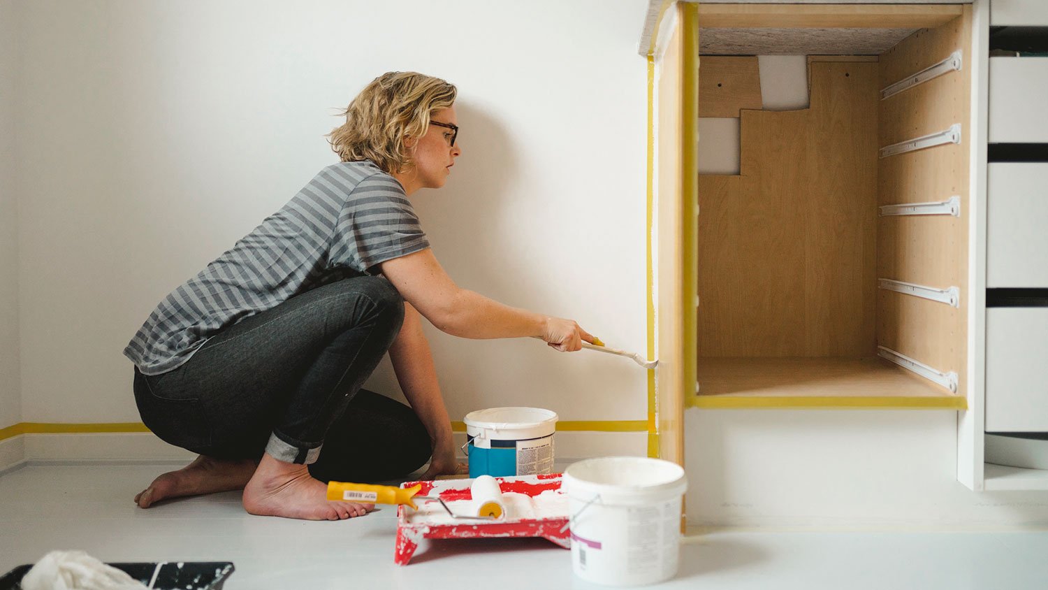 Woman sitting on the floor painting lower kitchen cabinets