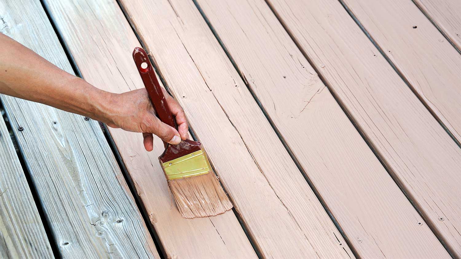 A hand paints a wooden deck