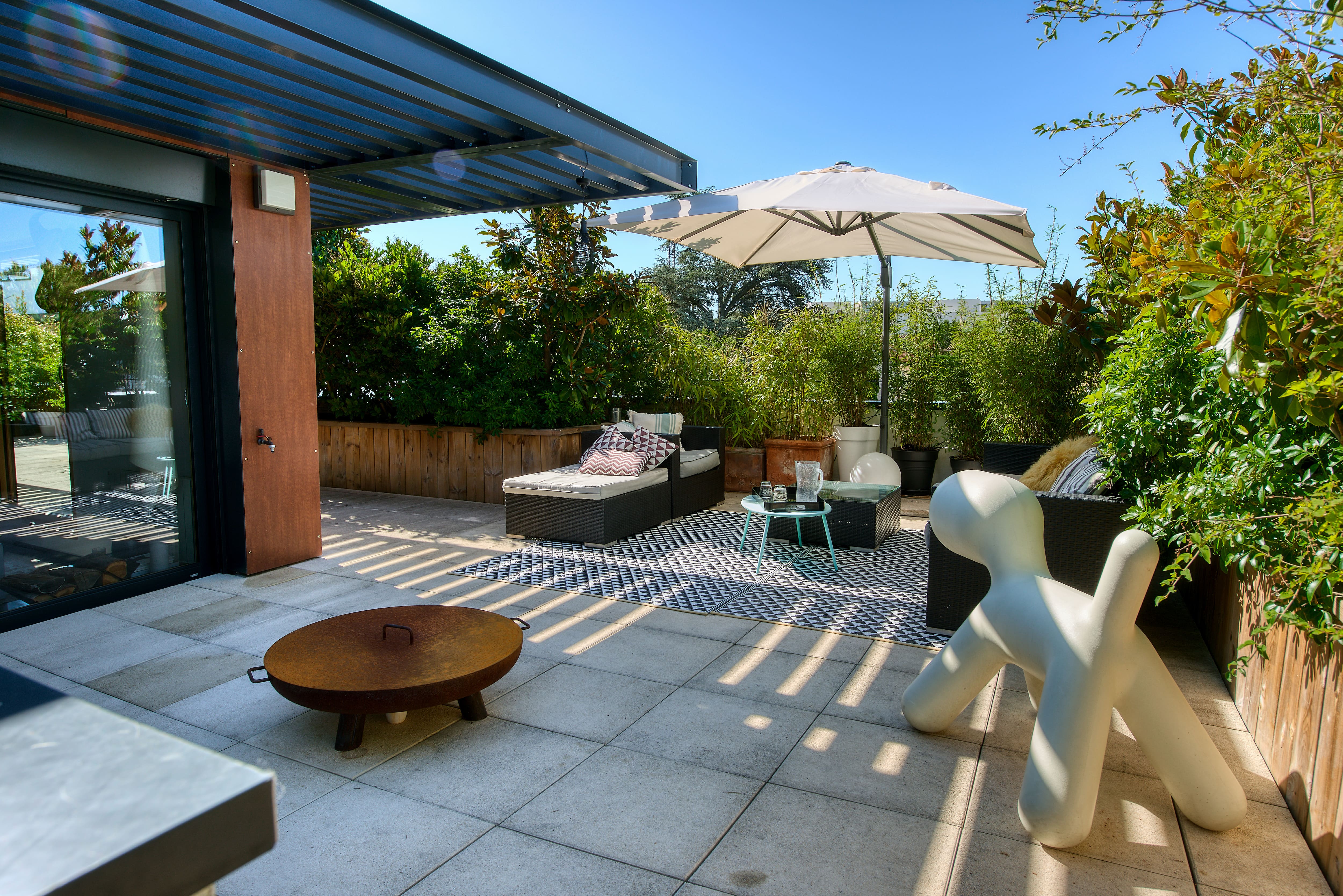 A patio area with a parasol cover, building overhang, firepit, and assorted seating