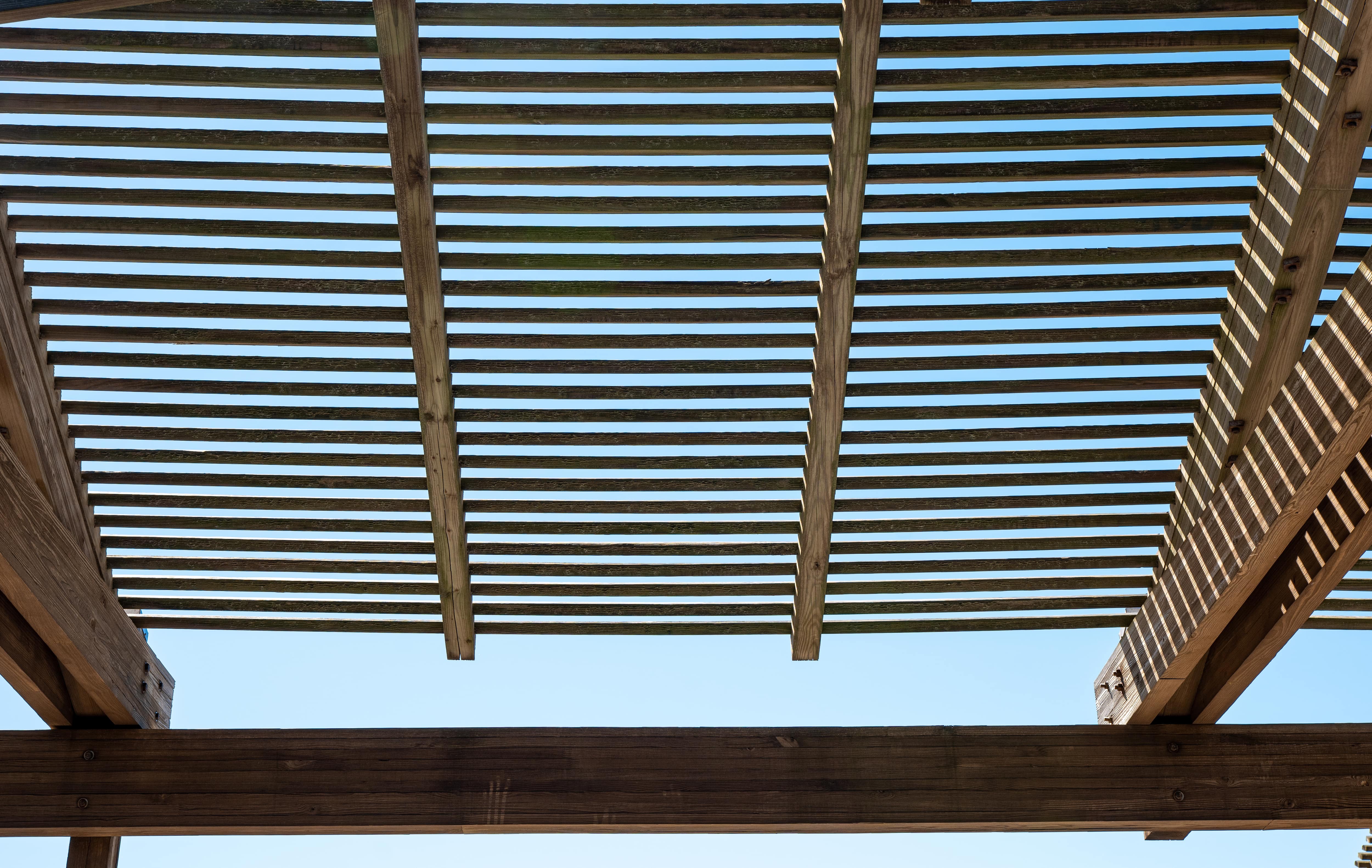 Roof of a horizontal slat pergola against a blue sky