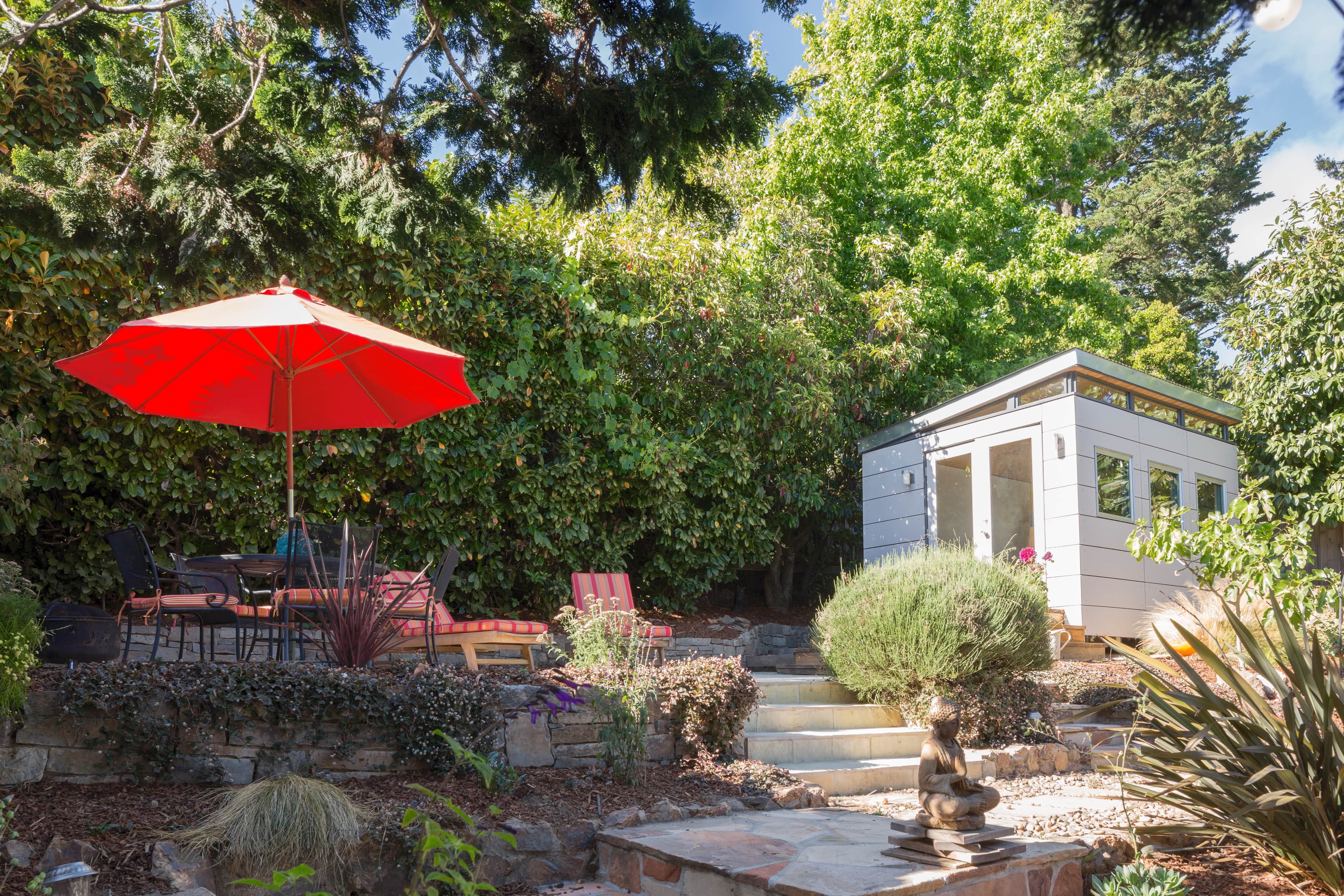 A patio shaded by trees with deck chairs and a red umbrella