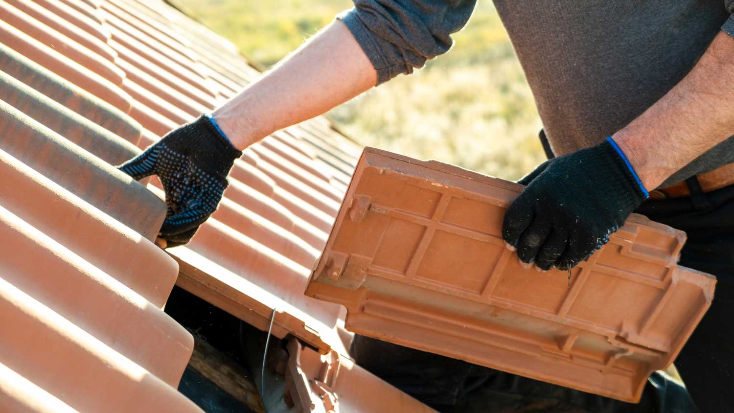 A person adding ceramic shingles to a roof