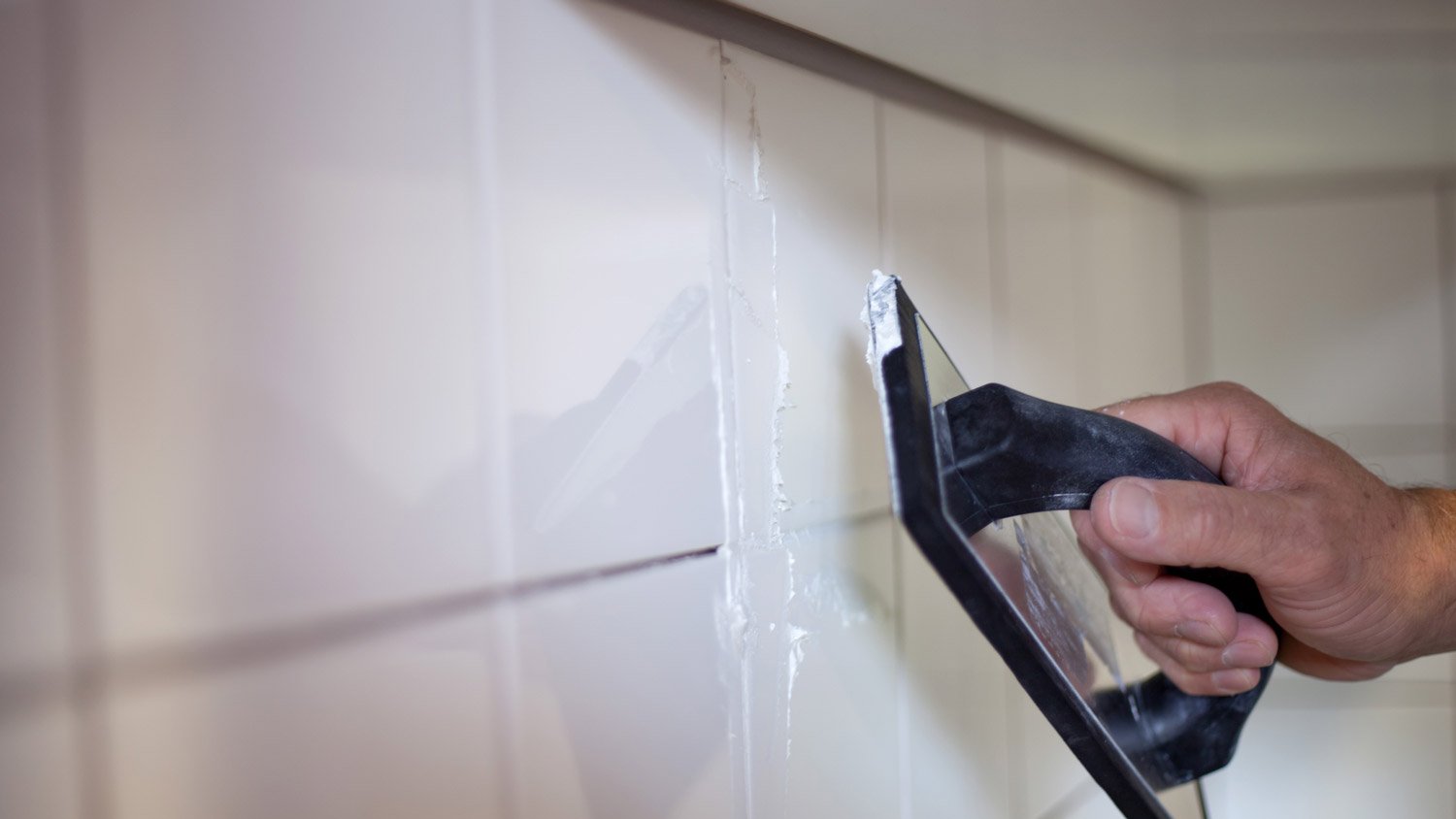 A person applying grout to the kitchen backsplash