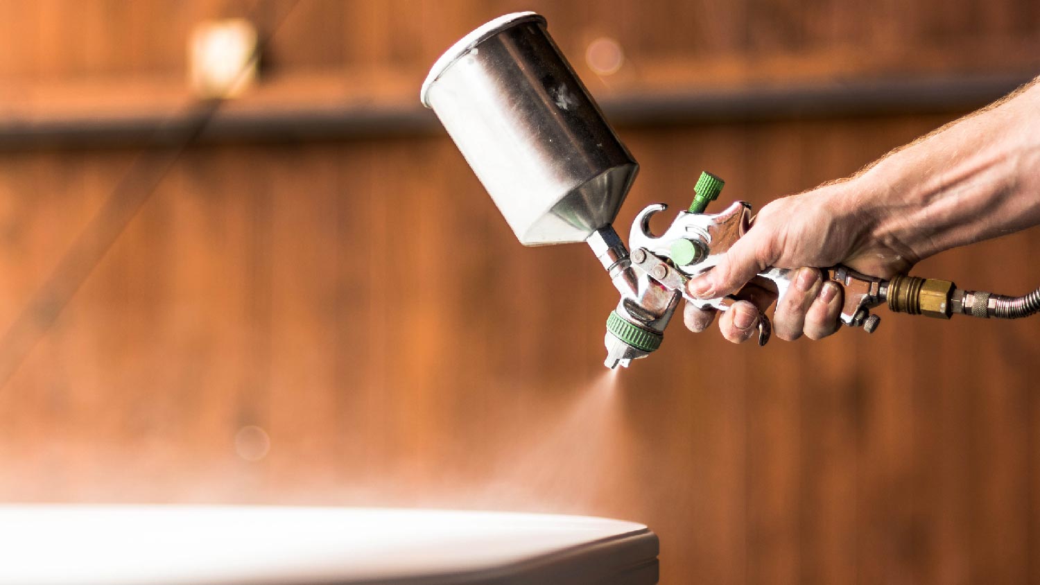 A person applying lacquer with a sprayer on a wooden surface