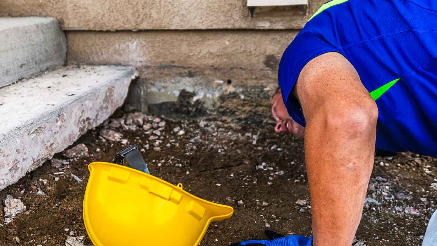 A person checking for soil erosion at a house’s foundation