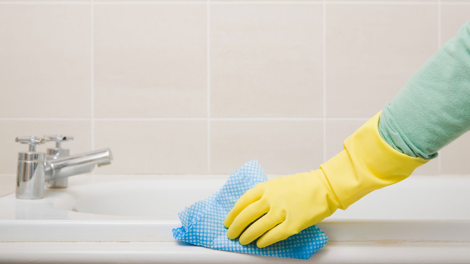 A person wearing protective gloves cleaning a bathtub