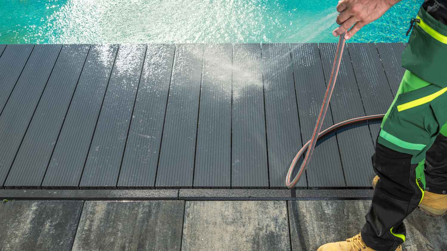 A person cleaning a composite deck next to a pool