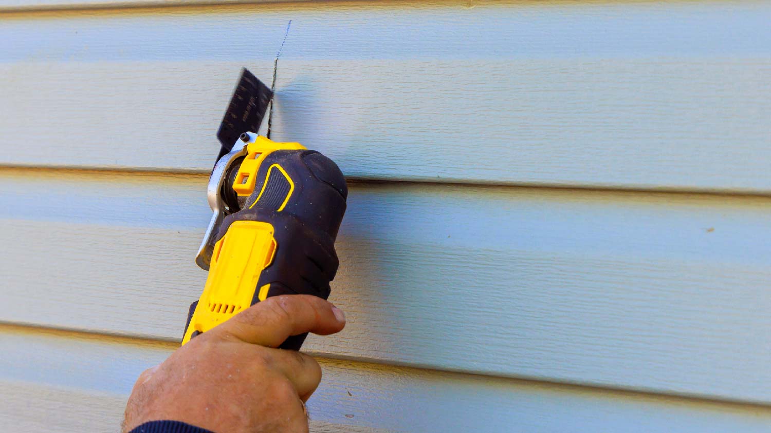A person cutting siding to replace it 