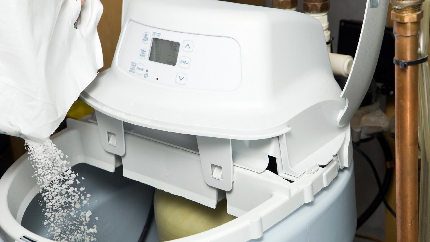A person filling a water softener tank with salt