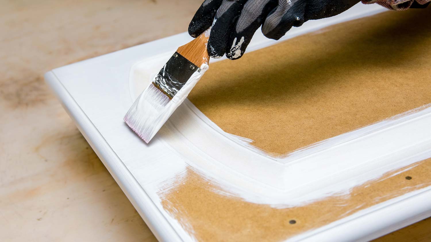 A person’s hand in gloves while painting a cabinet with a brush