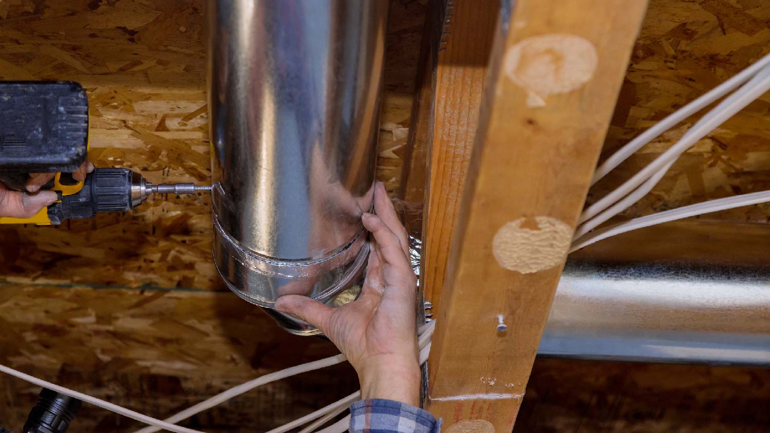 A person installing ductwork in a crawl space