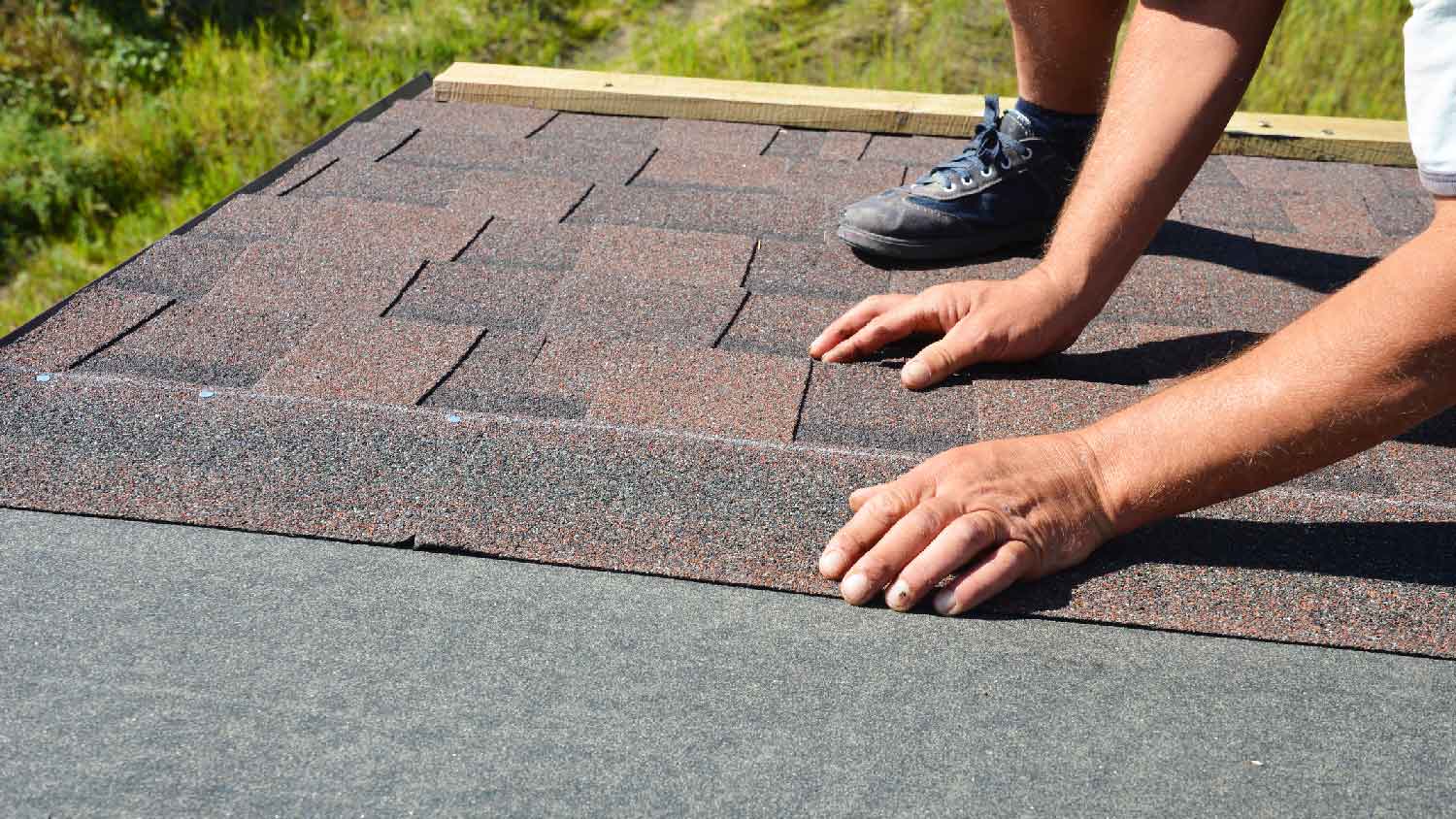 A person installing shingles on top of roof underlayment