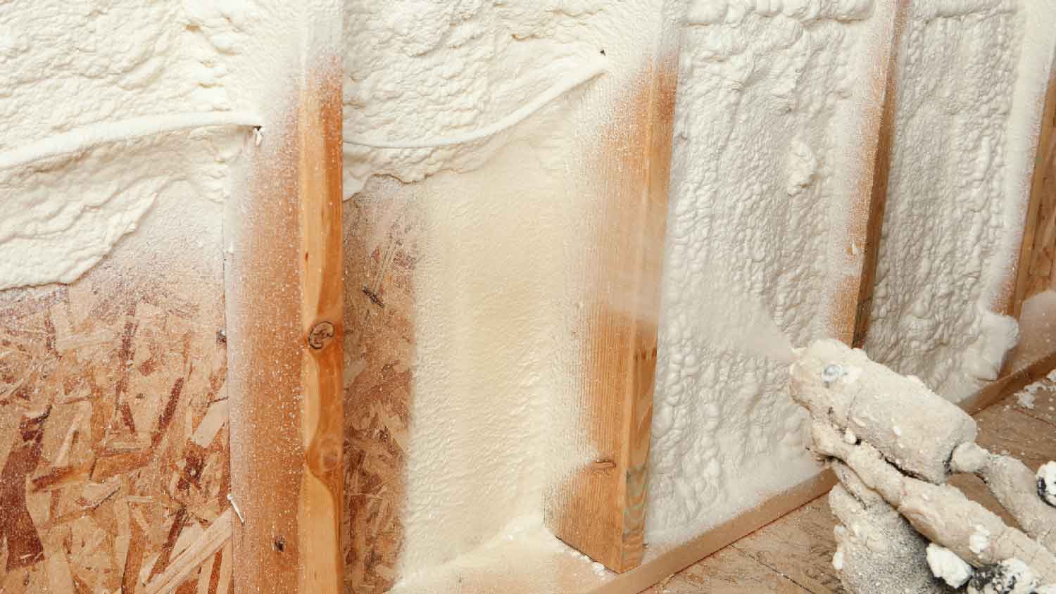 A person insulating between studs with spray foam insulation