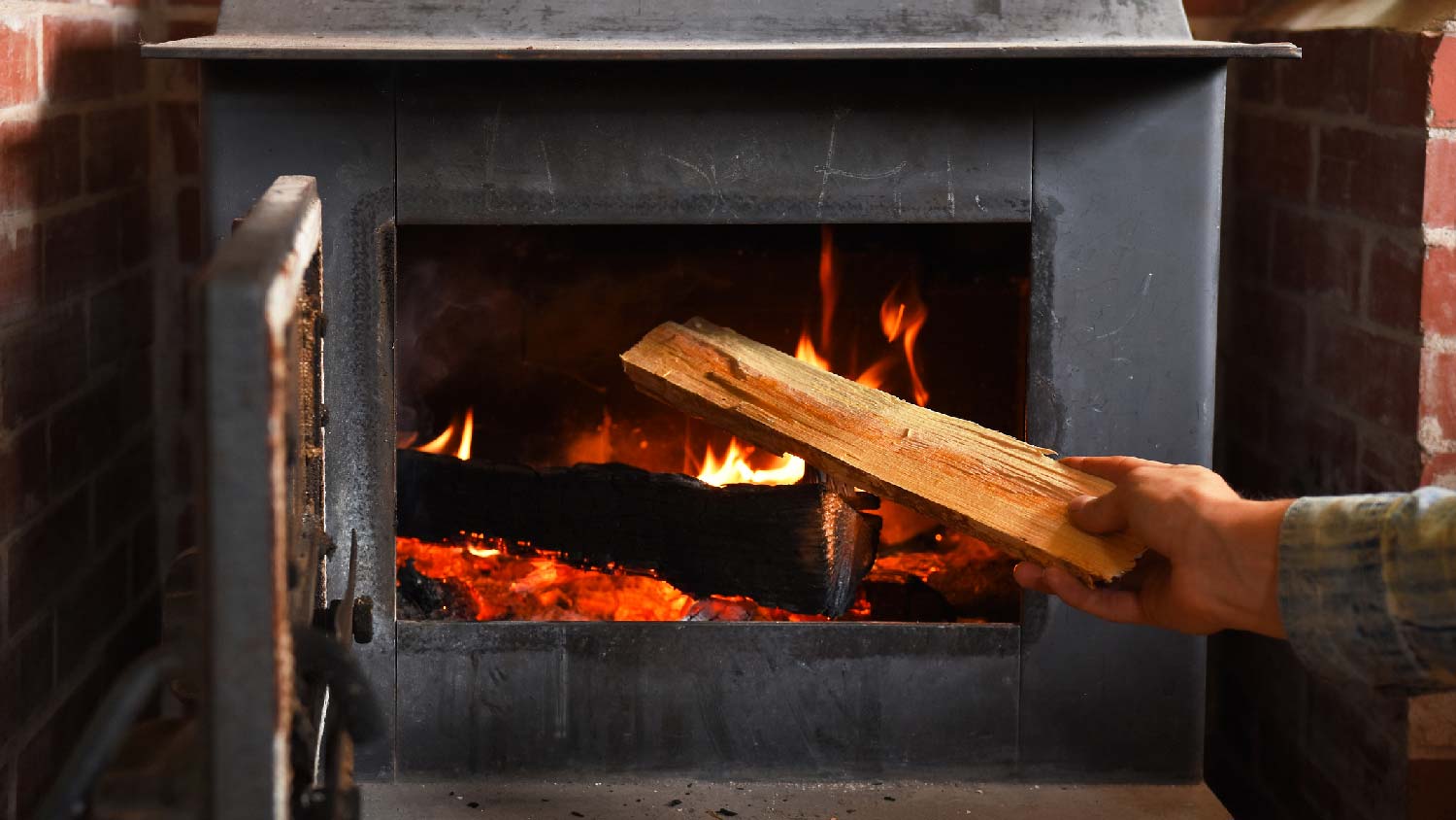 A person putting a log in a cast iron wood stove