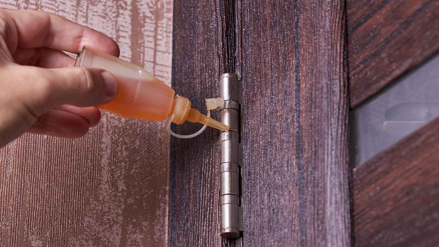 A person lubricating a door hinges