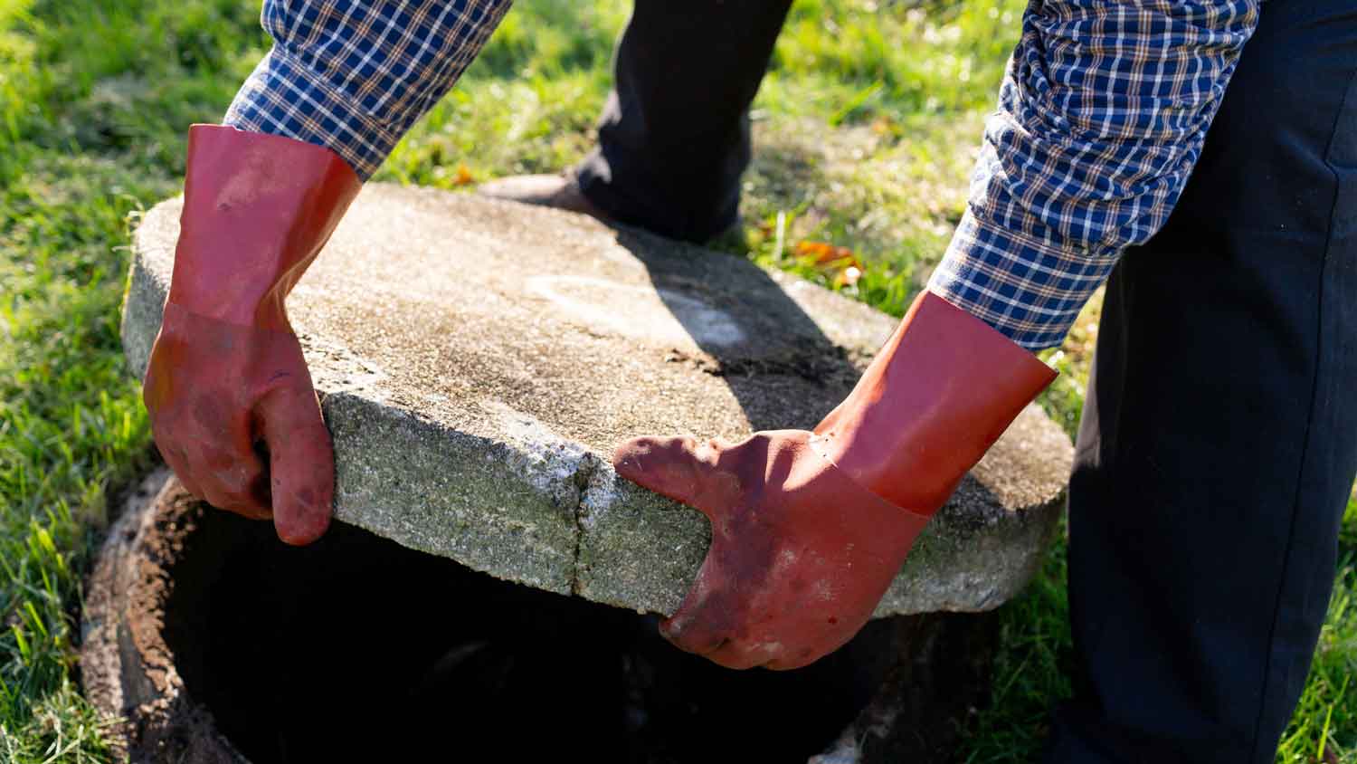 A person wearing protective gloves opening a septic tank