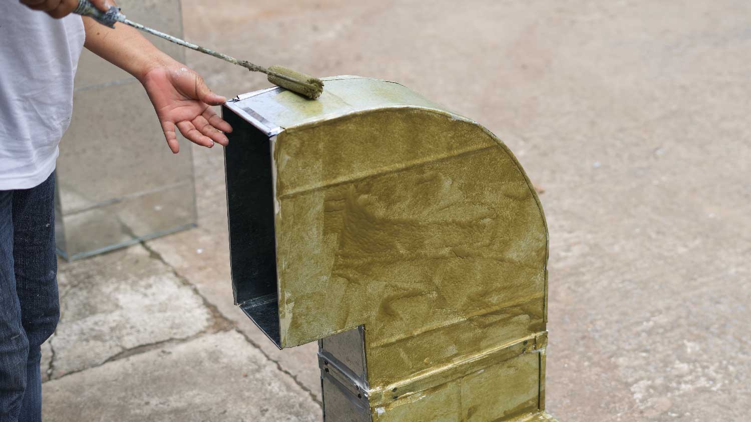 A person painting ductwork with a roller 