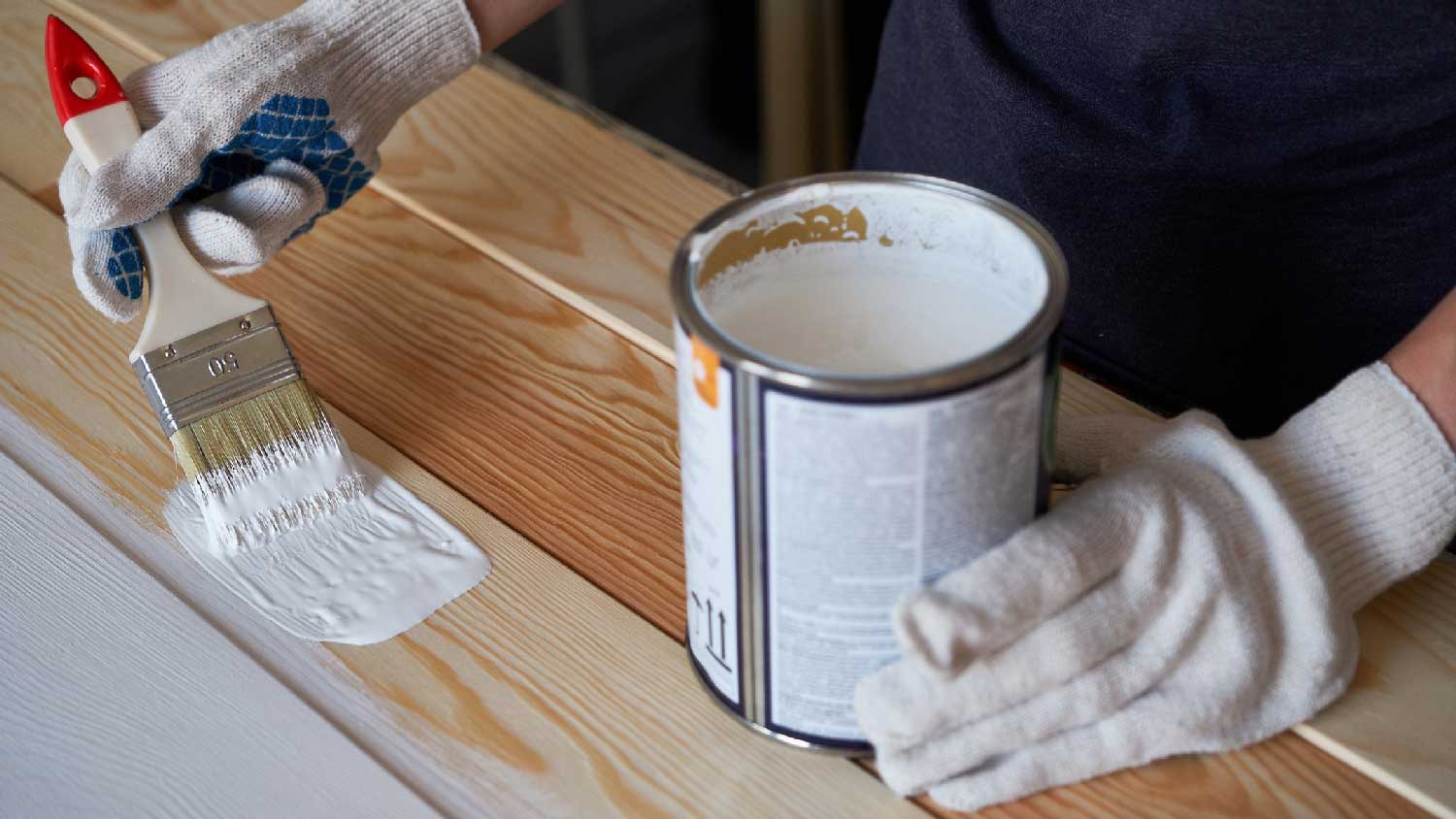 A person painting with a brush some pressure treated wood 