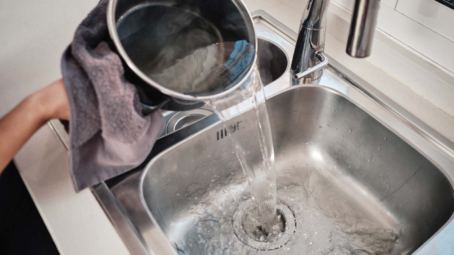 A person pouring boling water in the sink