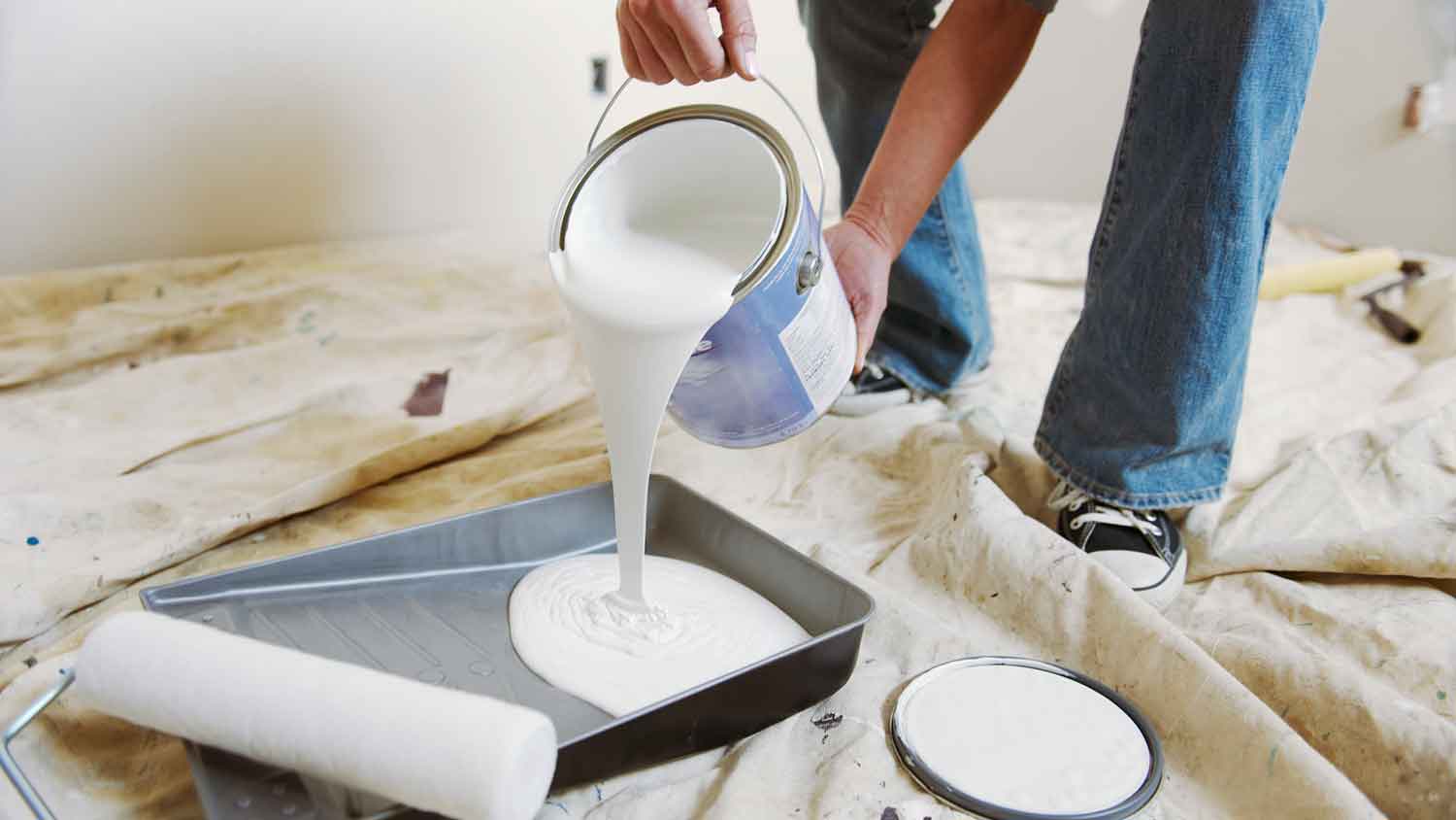 Person pouring paint into a paint tray sitting on the floor