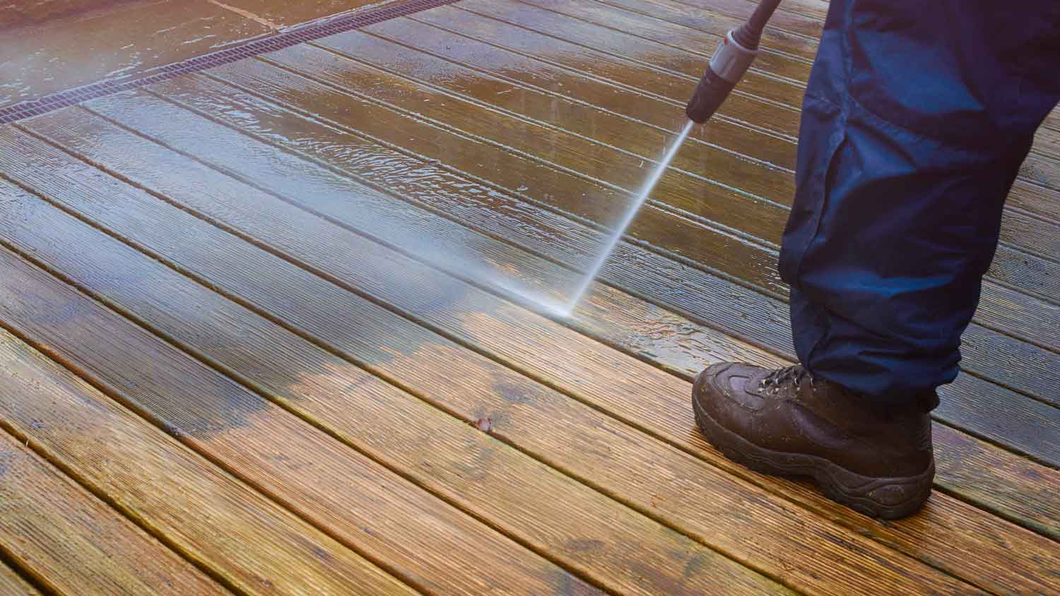 A person wearing protective boots pressure washing a deck