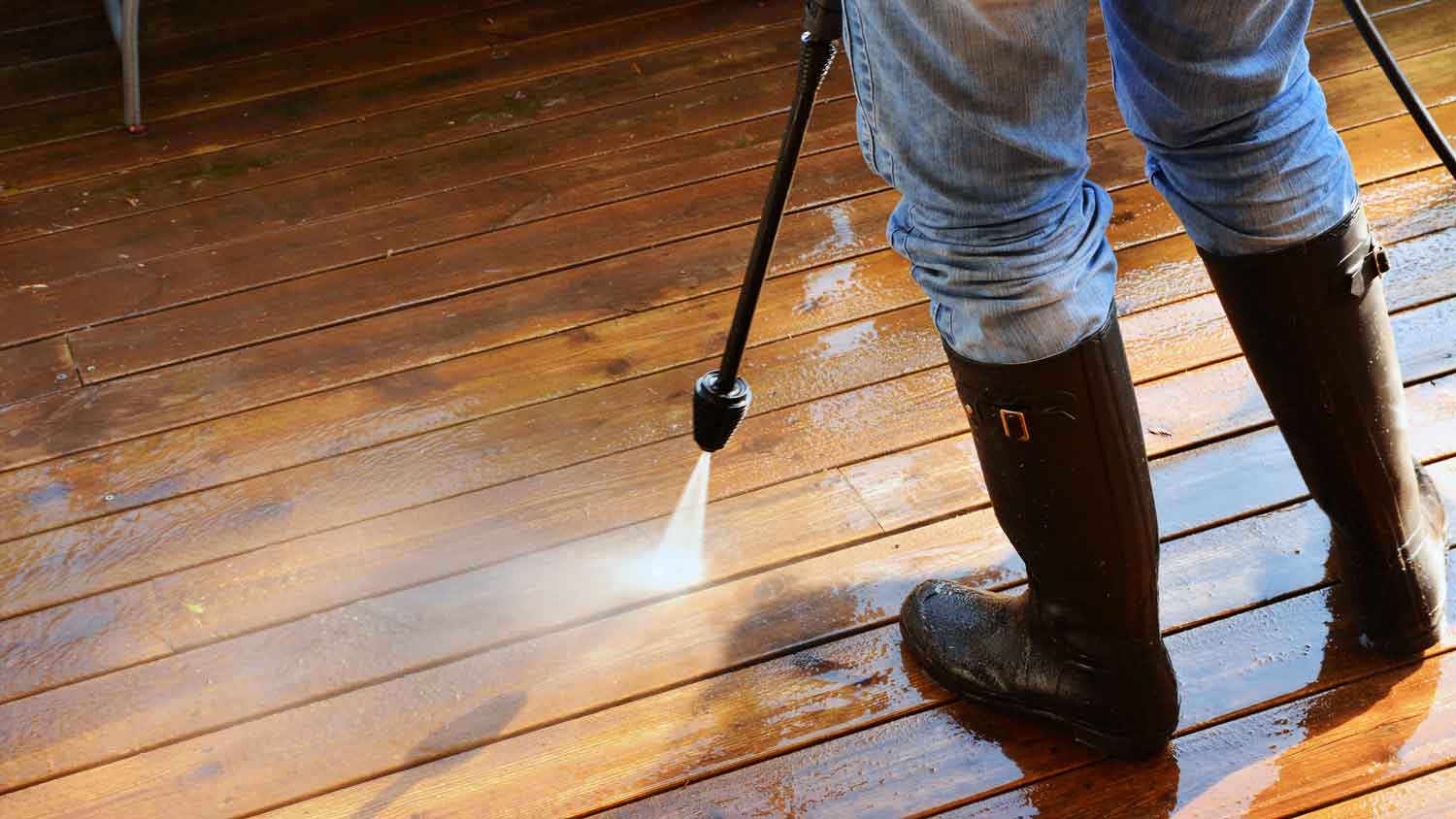 A person pressure washing a wooden patio