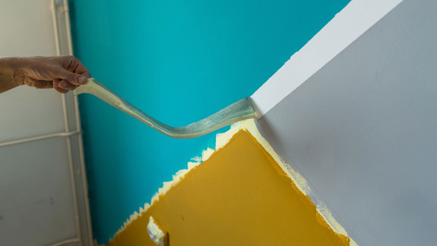 A person removing masking tape from painted wall