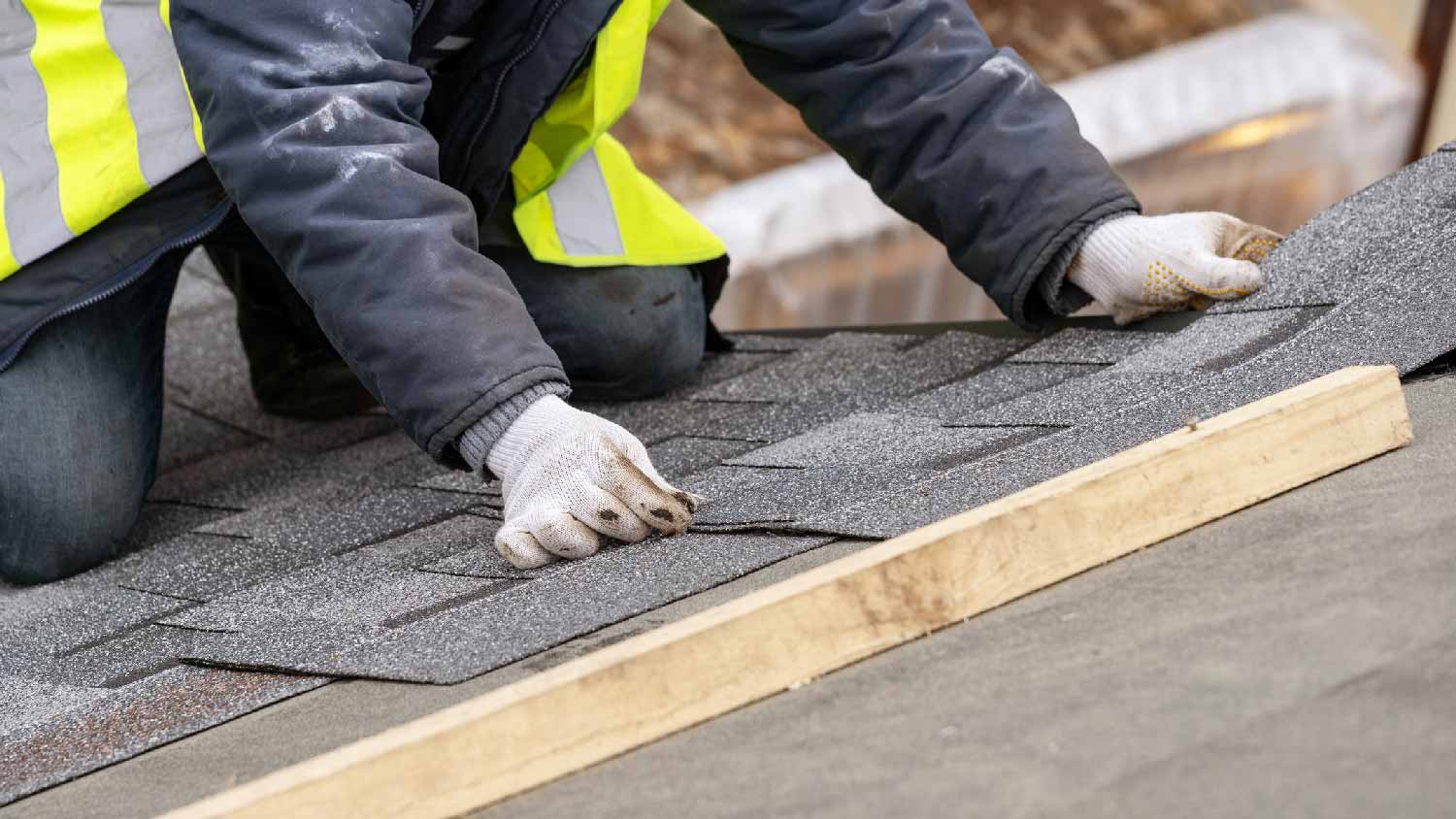 A person repairing damaged shingles with new ones