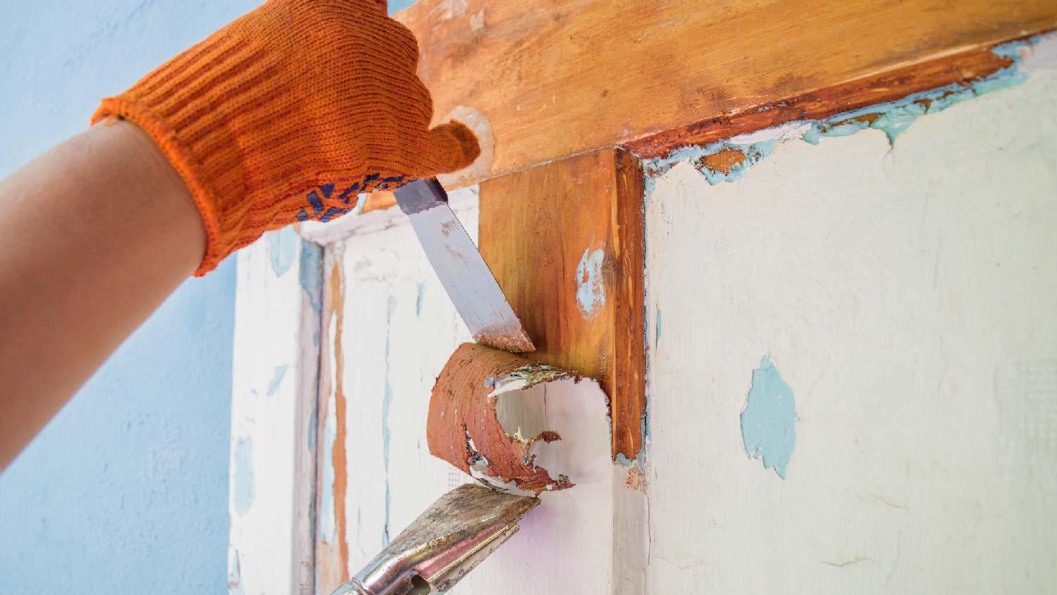 A person scraping off old paint from a wooden surface