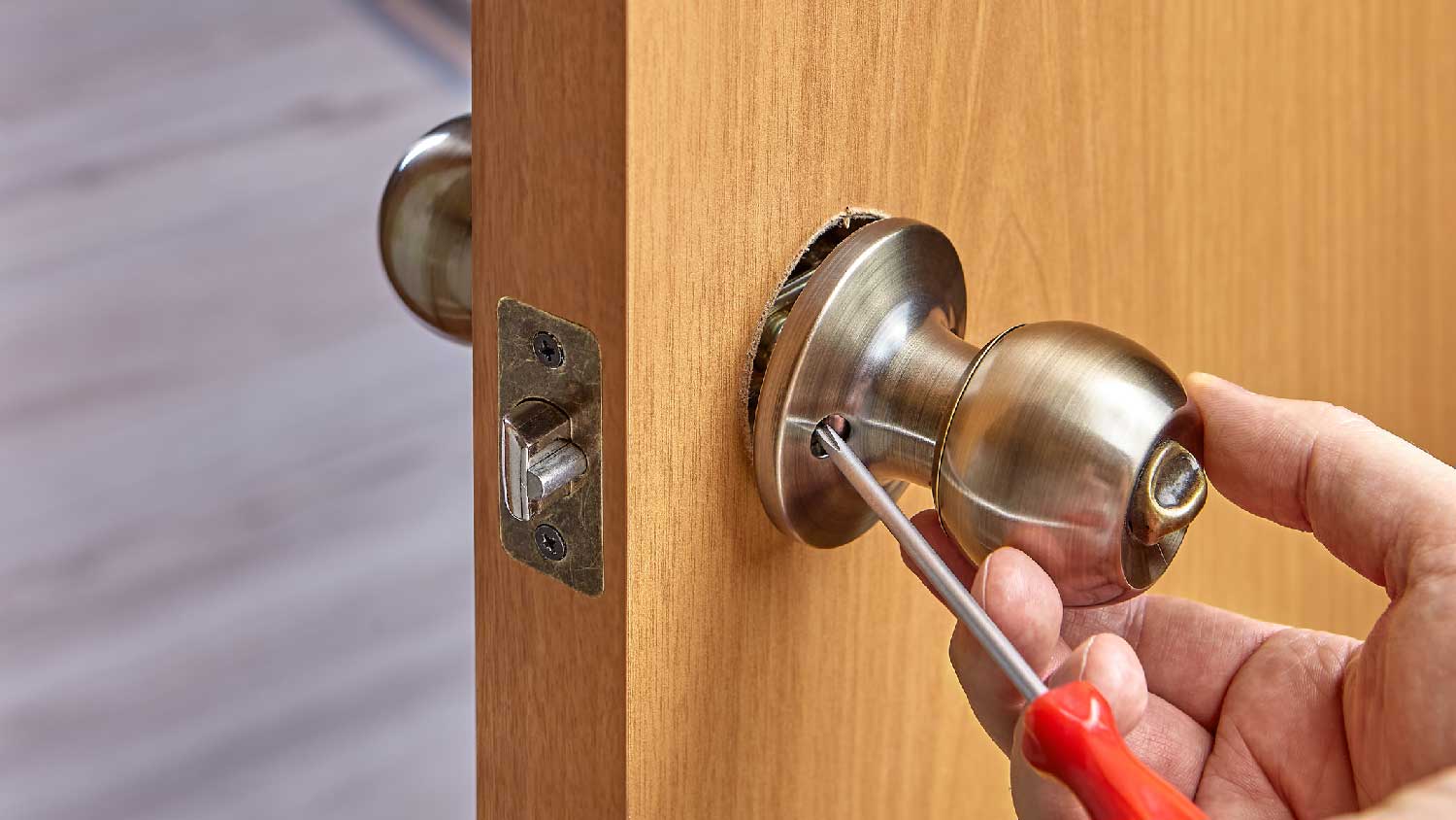 A person using a screwdriver to tighten a door knob