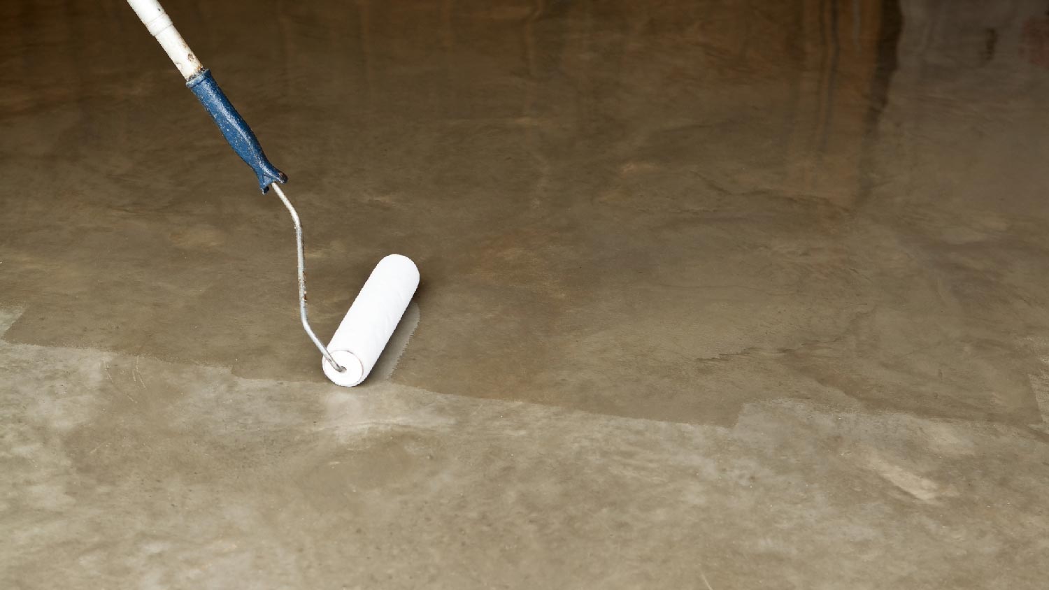 A person sealing a concrete surface with a roller