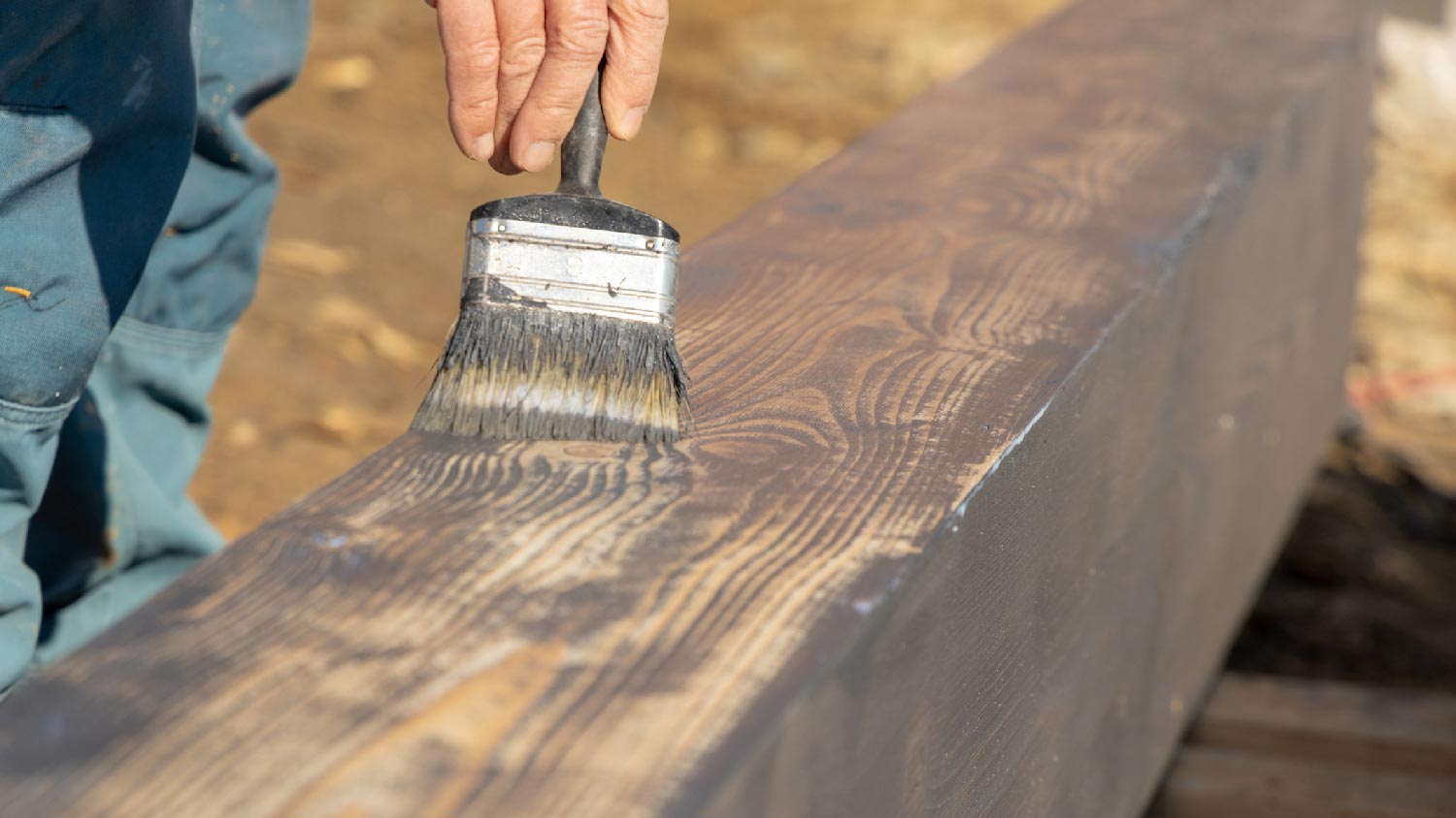 A person staining timber with a brush