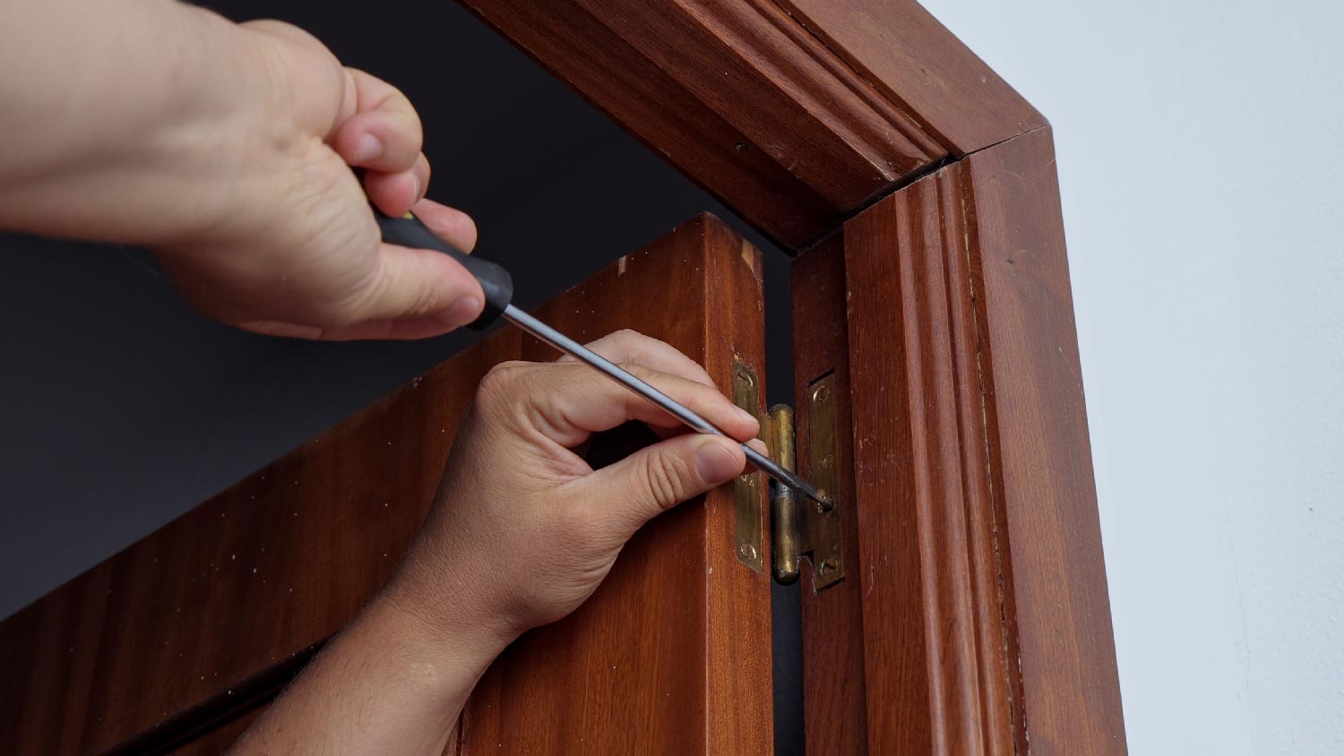 A person tightening a door hinge